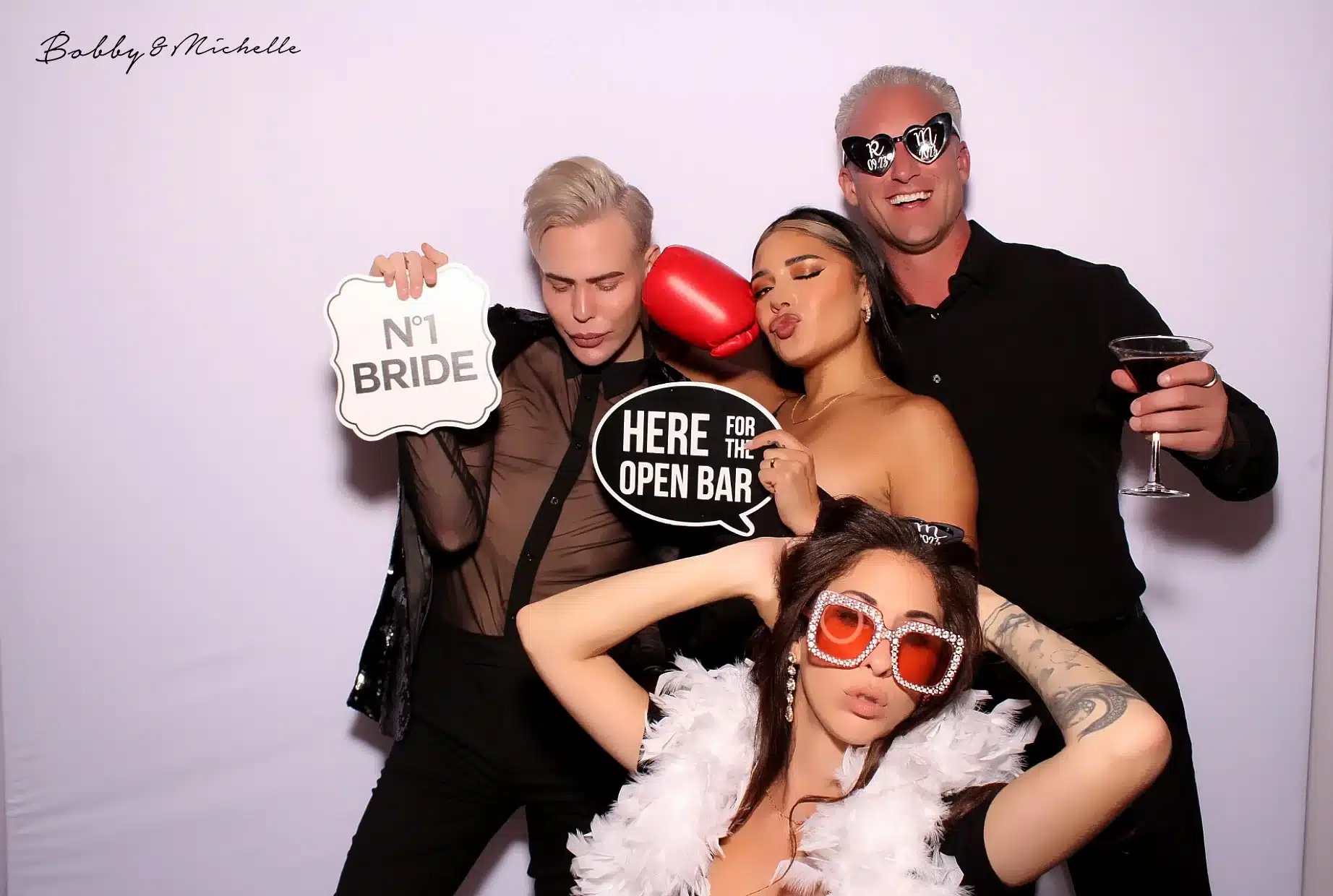 image of four friends posing with drinks sunglasses and a feather boa in a photobooth